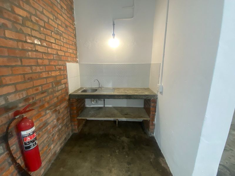 A functional utility area featuring a concrete countertop, integrated sink, tiled splashback, and exposed brick wall finish.