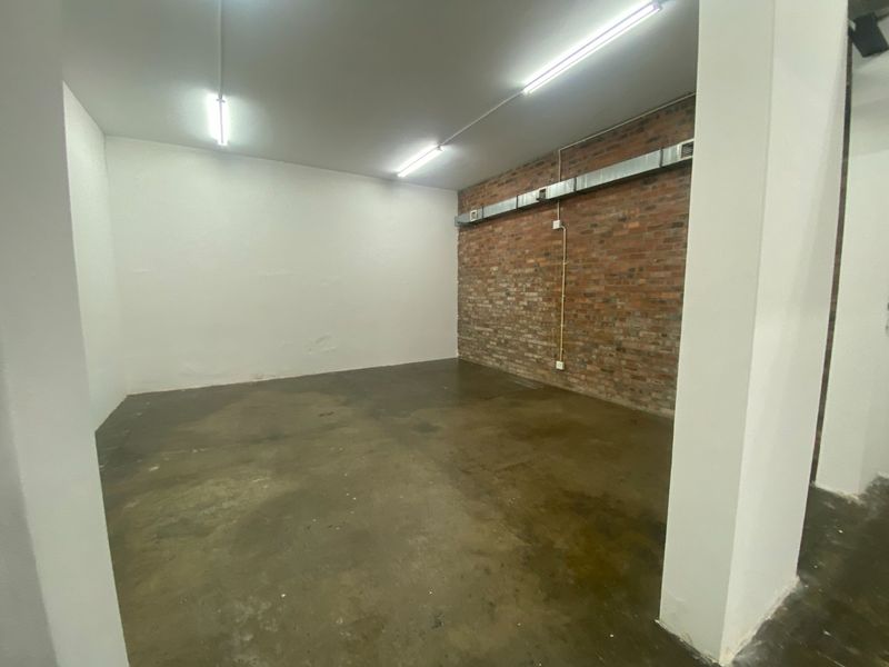An empty industrial utility space featuring exposed brickwork, concrete flooring, and functional overhead fluorescent lighting with exposed ventilation ducting.