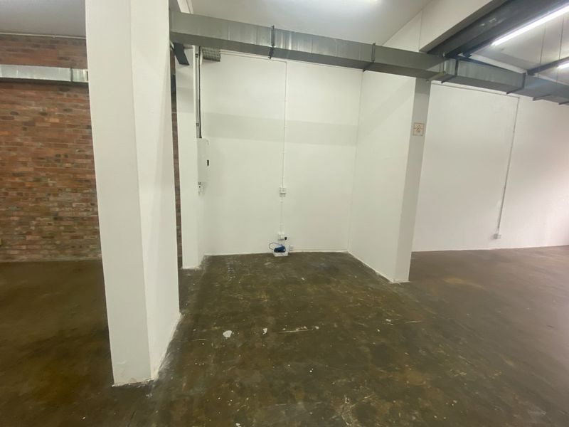 An open-plan industrial utility space featuring exposed brickwork, concrete flooring, and exposed overhead ducting, suitable for storage or workshop use.