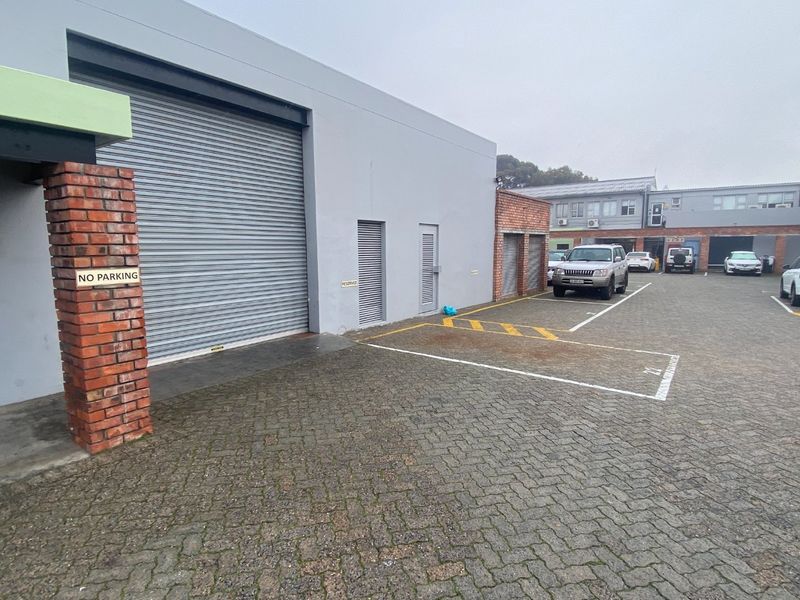 Industrial property exterior featuring a large roller shutter door, brick pillar detailing, and designated paved parking bays.