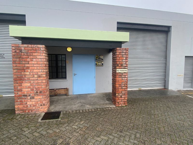 Industrial unit entrance featuring a covered porch with brick pillars, roller shutter doors, and paved driveway access.