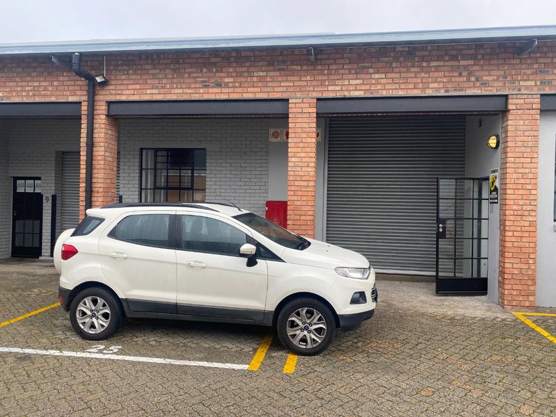 Industrial unit exterior featuring a brick facade, roller shutter door, and dedicated paved parking bay.