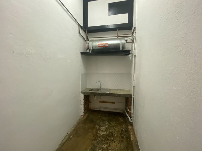 A functional utility space featuring a stainless steel sink, wall-mounted geyser, and exposed plumbing, suitable for industrial or workshop use.