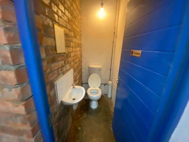 A compact industrial-style restroom featuring exposed brick walls, a wall-mounted basin, and a standard toilet with exposed plumbing.