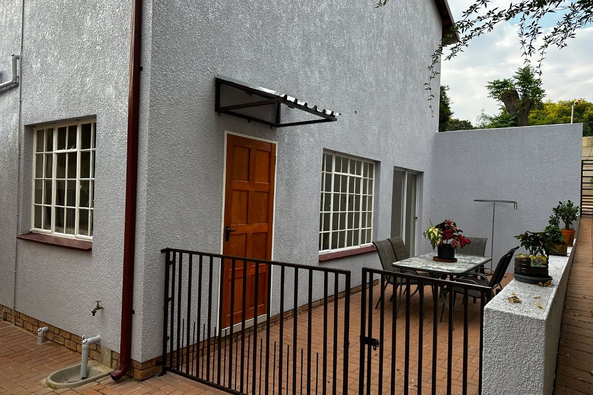 Rear exterior view of the apartment featuring a paved patio area, secure metal gate, timber door, and steel-framed windows with a protective awning.