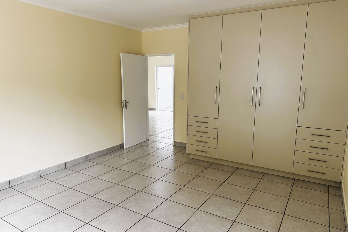 A spacious, empty bedroom featuring neutral tiled flooring and extensive built-in cupboard storage with a clean, minimalist aesthetic.