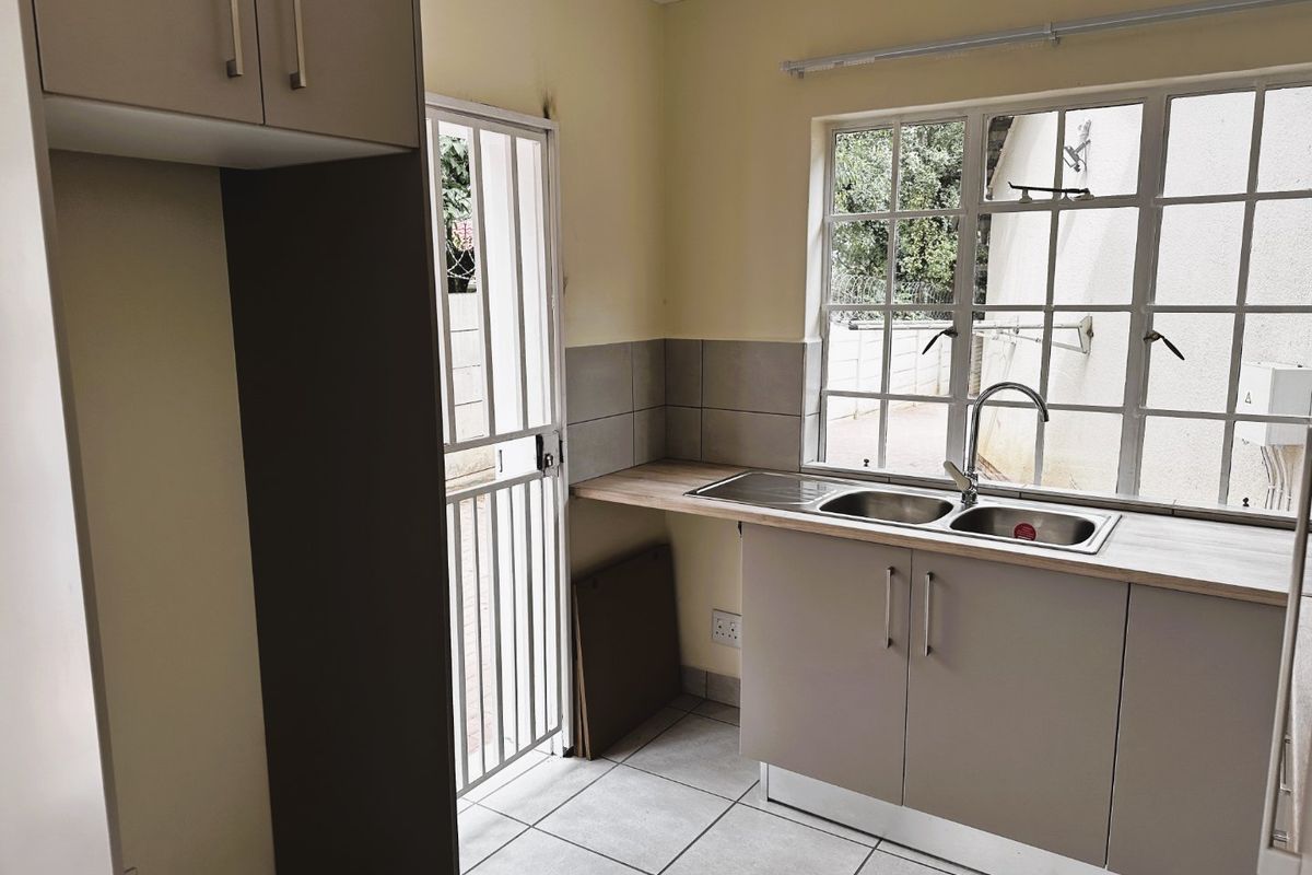 A functional kitchen area featuring built-in cabinetry, a double bowl sink, tiled flooring, and direct access to an outdoor area via a security gate.