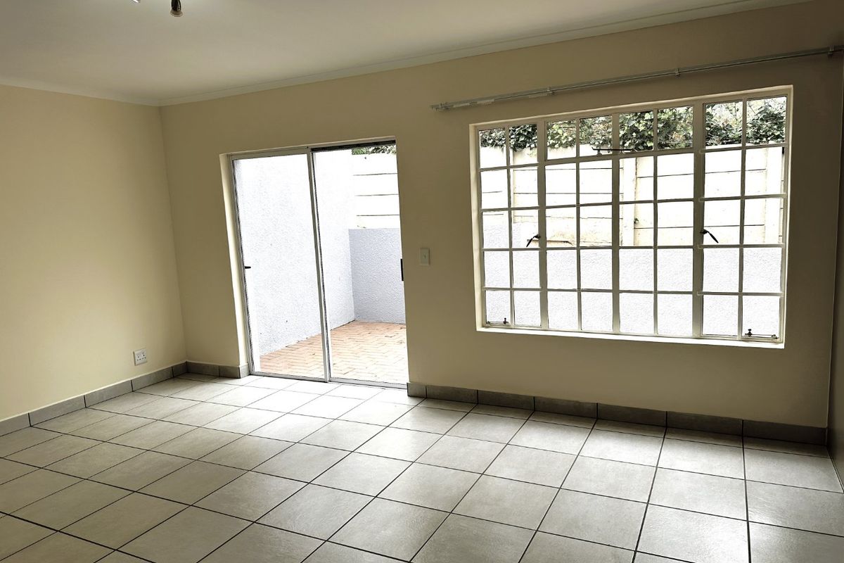 A bright, empty living area featuring neutral tiled flooring, track lighting, and direct access to a private outdoor patio through a sliding glass door.