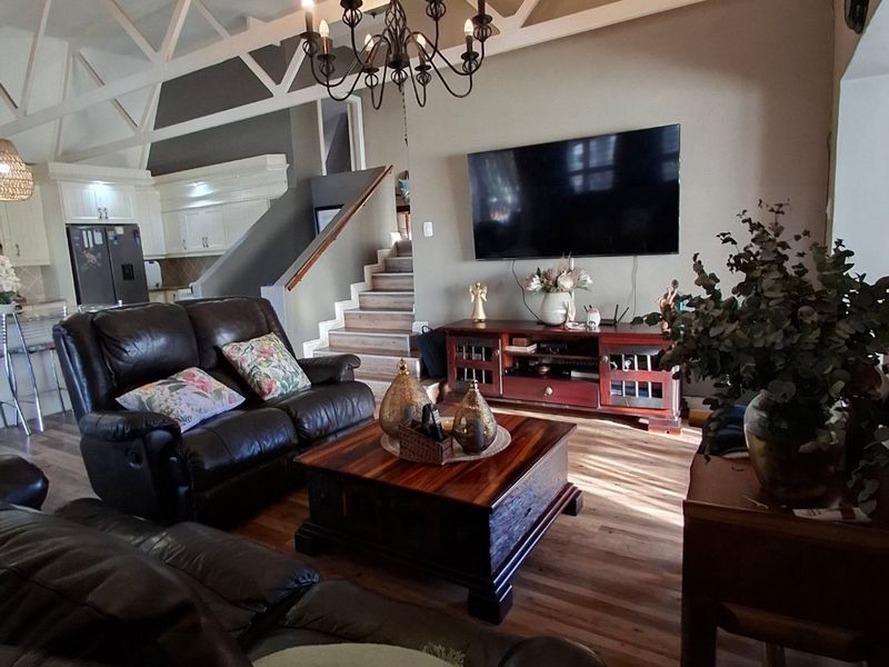 Spacious open-plan living area featuring high vaulted ceilings with exposed white trusses, laminate flooring, and an integrated kitchen visible in the background.