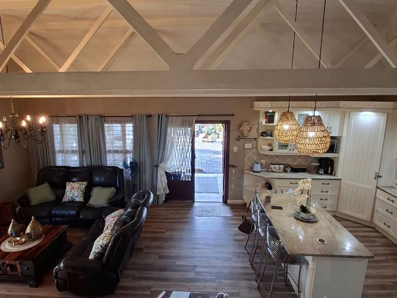 Spacious open-plan living area featuring high vaulted ceilings with exposed trusses, a modern kitchen with island, and seamless flow to the outdoor entrance.