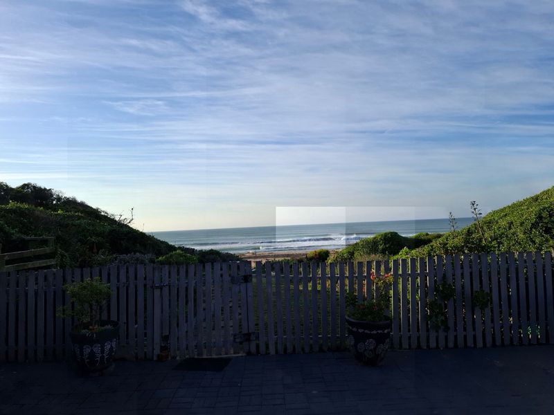 A scenic view of the ocean and coastline from a paved patio area enclosed by a wooden picket fence.