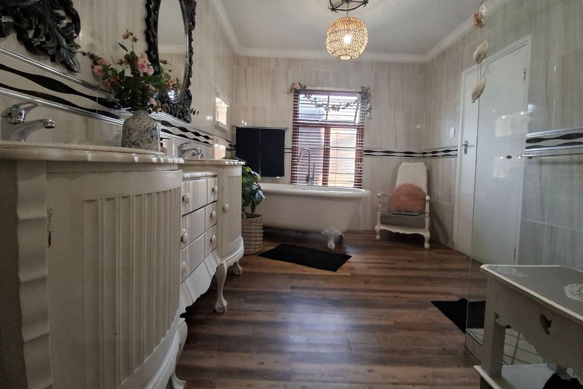 A well-maintained bathroom featuring a classic clawfoot bathtub, double vanity unit, and neutral wall tiling with wood-look laminate flooring.