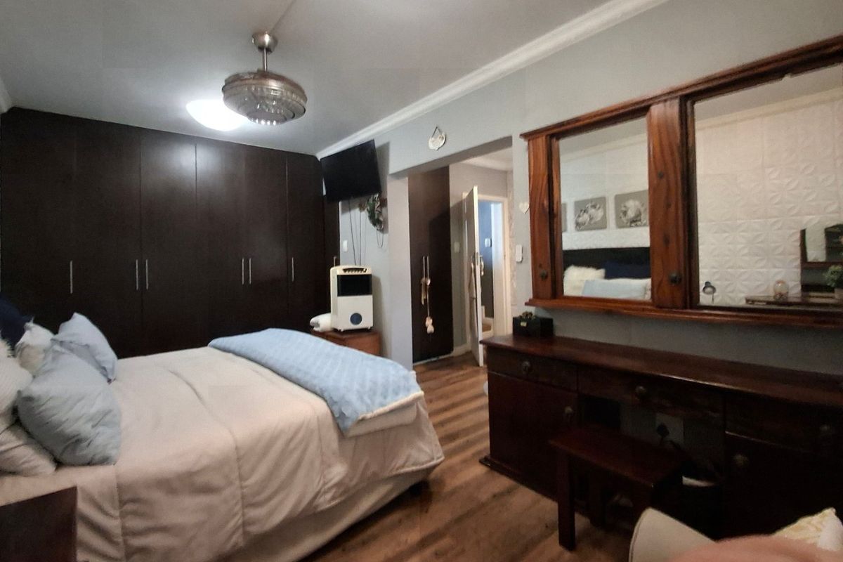 Spacious bedroom featuring dark wood built-in cupboards, laminate flooring, and a ceiling fan, offering a functional layout with ample storage space.