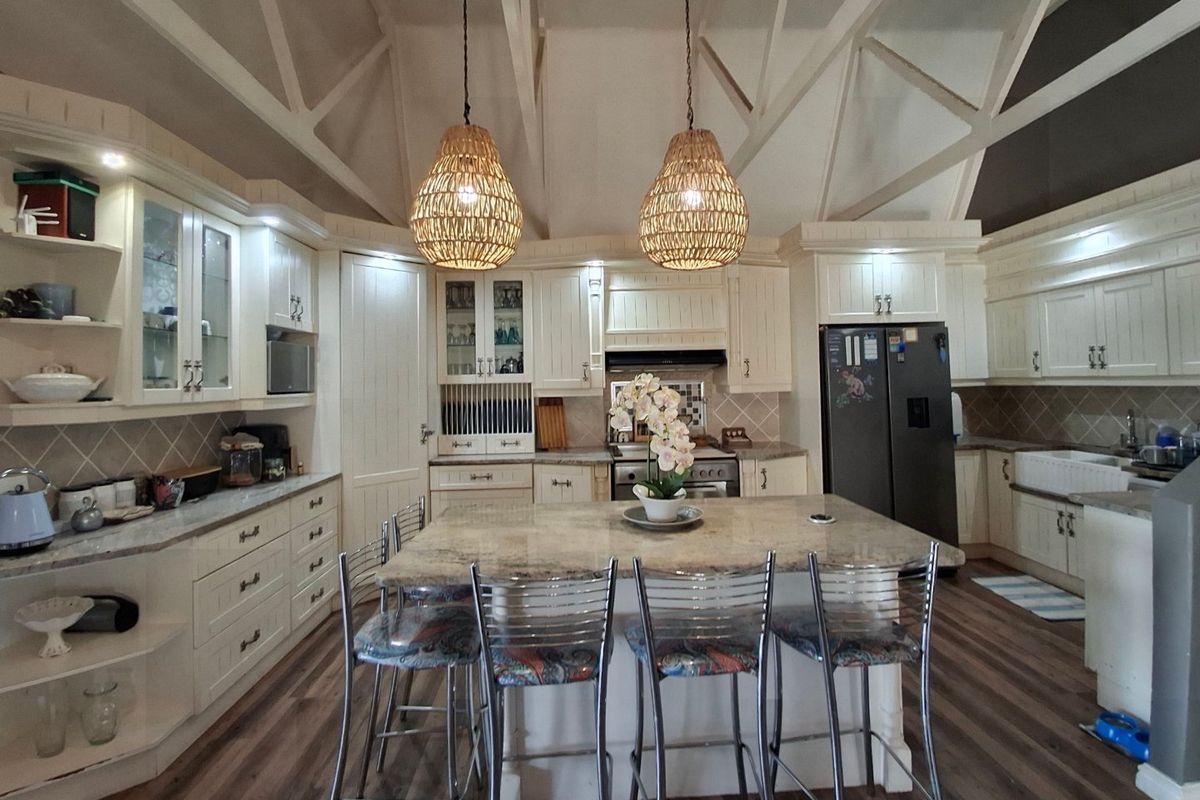 Spacious kitchen featuring a large central island with granite countertops, farmhouse sink, extensive cabinetry, and a striking vaulted ceiling with exposed trusses.