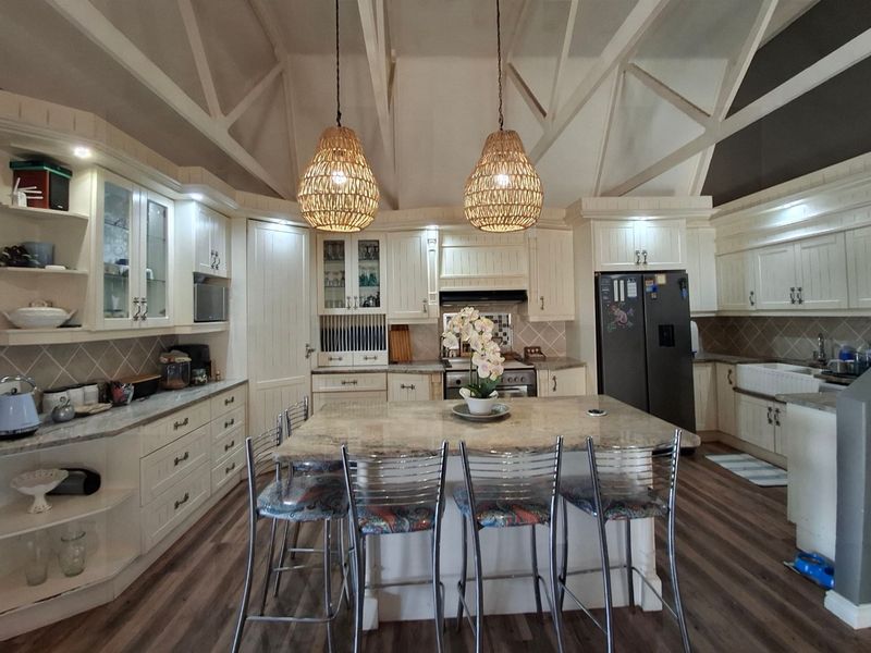 Spacious kitchen featuring a large central island with granite countertops, farmhouse sink, extensive cabinetry, and a striking vaulted ceiling with exposed trusses.