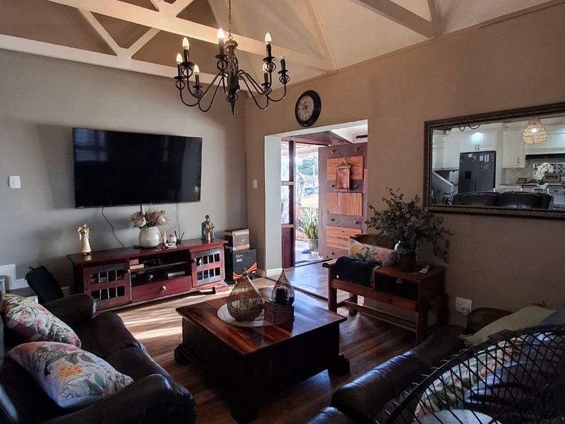 Spacious living room featuring a high vaulted ceiling with exposed beams, hardwood flooring, and a classic chandelier, creating a warm and inviting atmosphere.