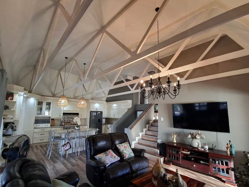 Spacious open-plan living area featuring high vaulted ceilings with exposed trusses, a modern kitchen with island, and a staircase leading to the upper level.