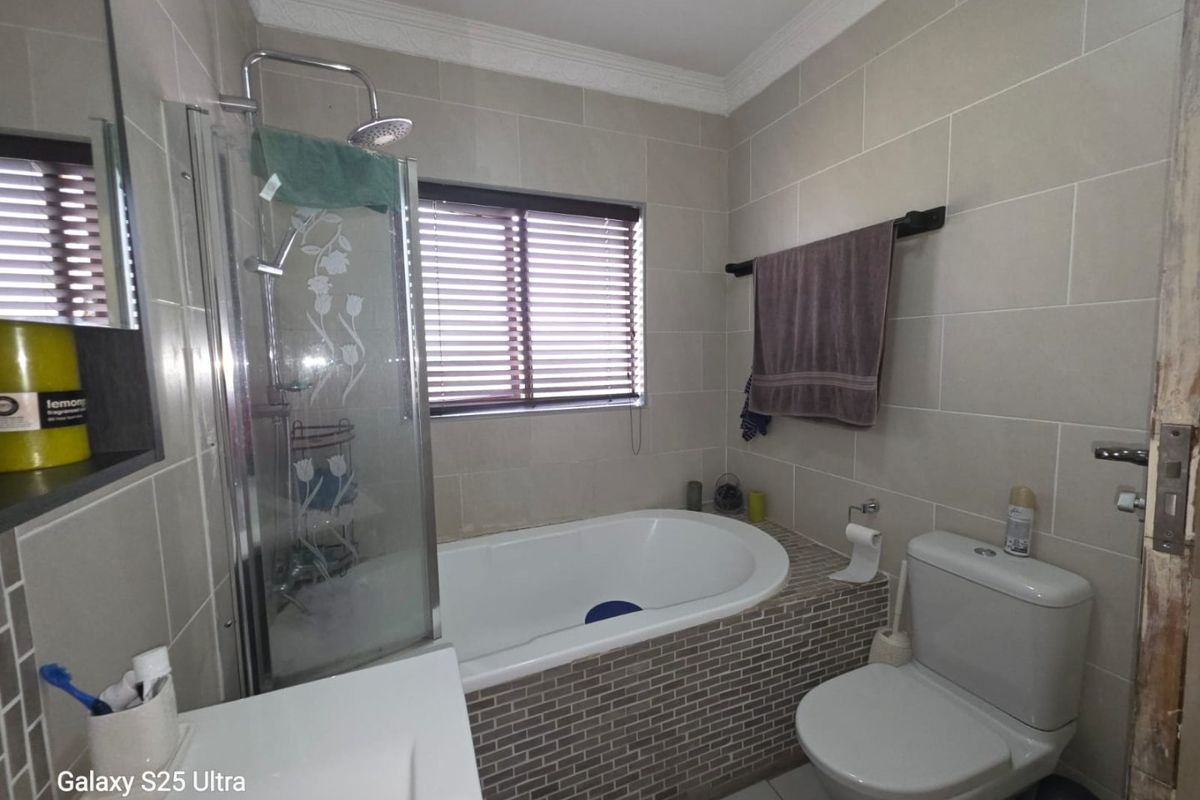 A functional bathroom featuring a built-in bathtub, separate shower enclosure, toilet, and vanity basin with neutral wall tiling.