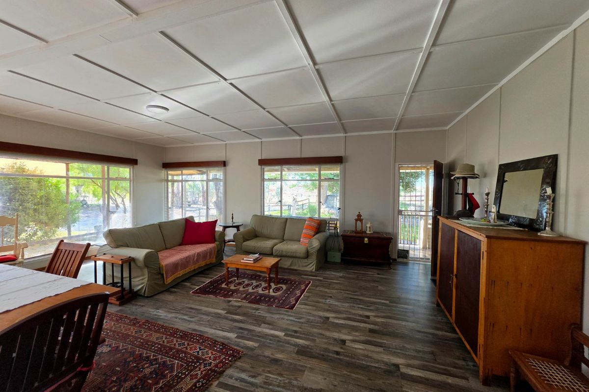Spacious living area featuring modern laminate flooring, large windows providing ample natural light, and a tiled ceiling finish.