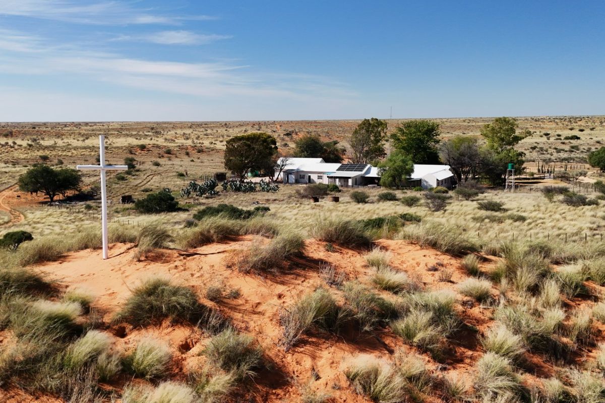 Aerial view of a rural farm property featuring a main dwelling with solar panels, water infrastructure, and surrounding arid landscape.