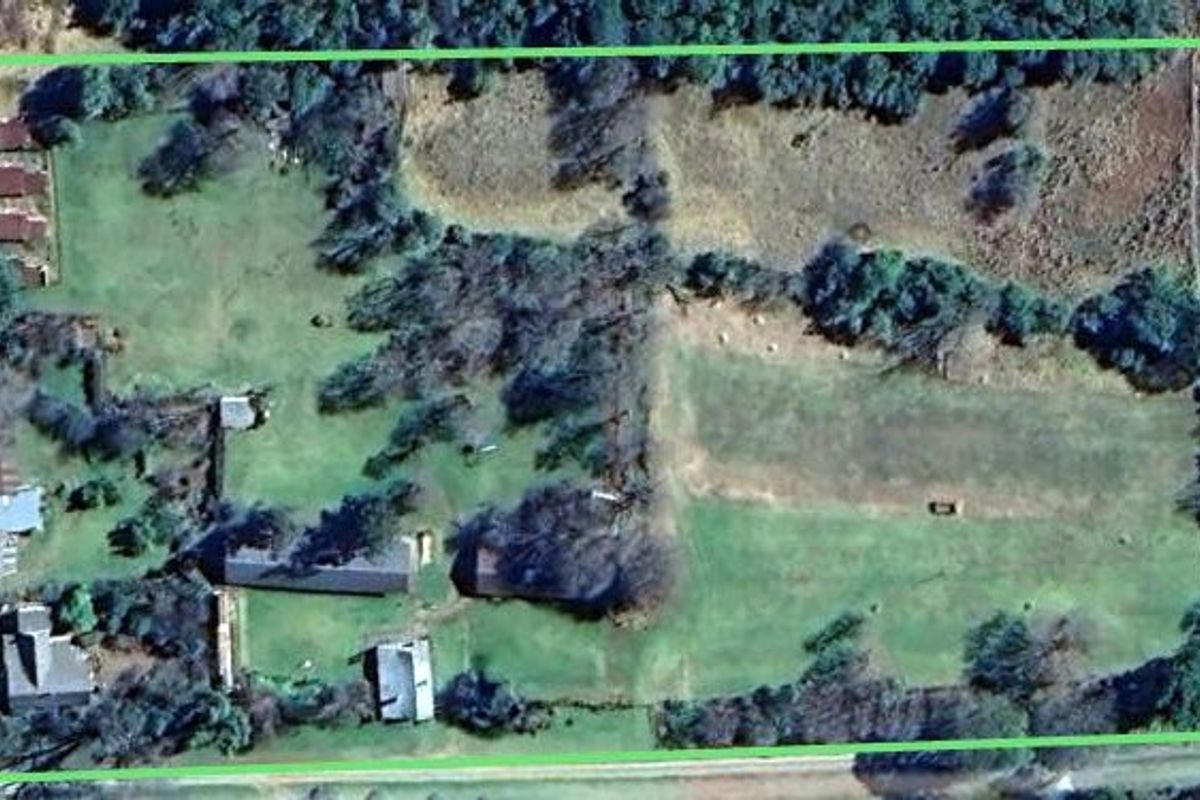 Aerial view of a large farm property featuring multiple outbuildings, a main dwelling, and expansive cleared land within a fenced perimeter.