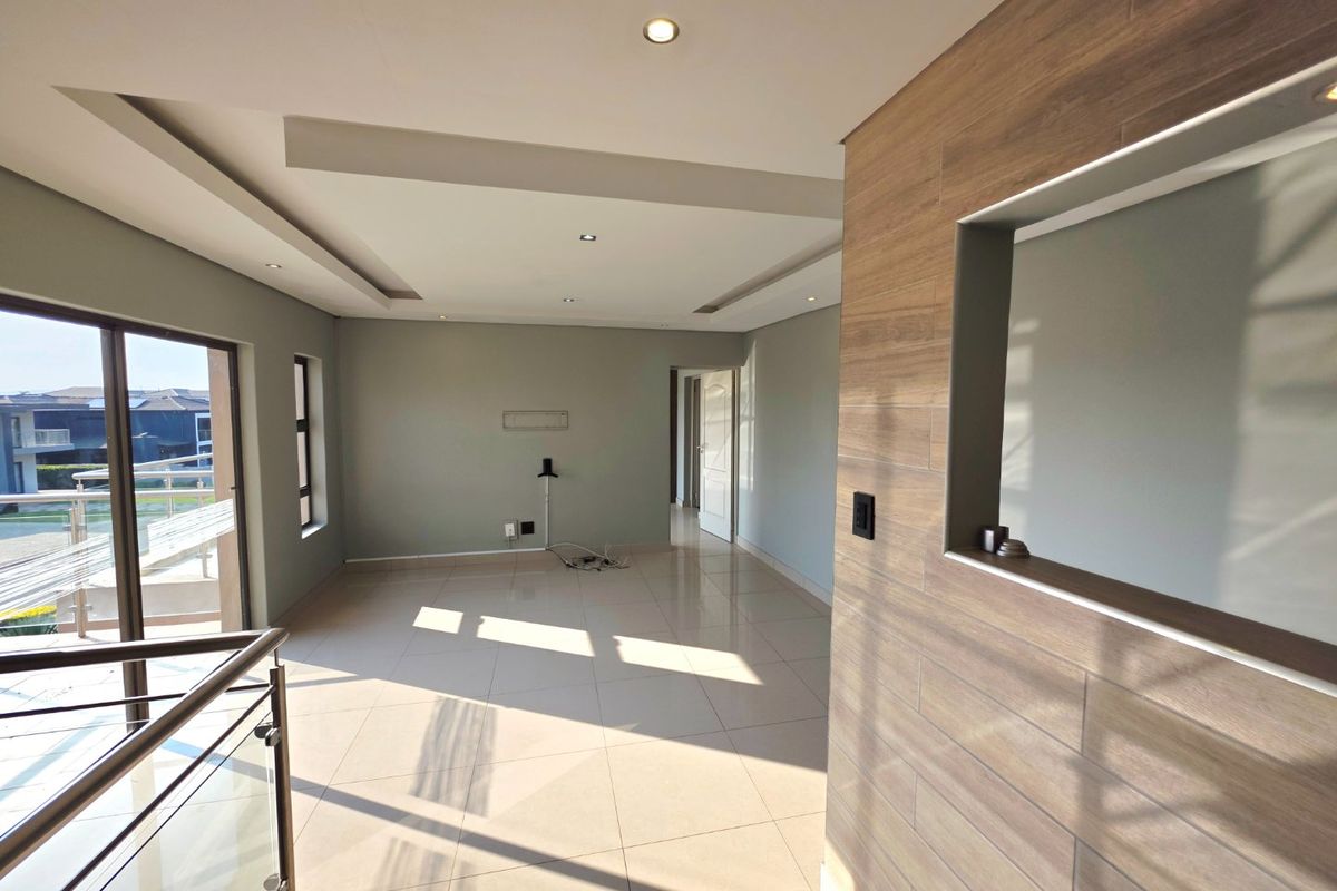 Spacious, light-filled living area featuring modern tiled floors, recessed ceiling lighting, and a stylish wood-look feature wall with access to an outdoor balcony.