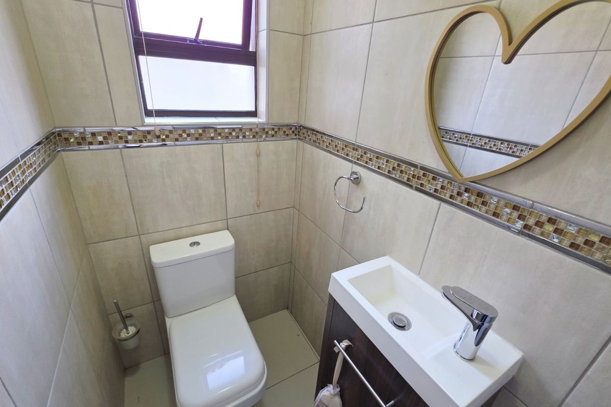 A compact, well-maintained guest bathroom featuring neutral wall tiles with a decorative mosaic border, a modern vanity basin, and a toilet.