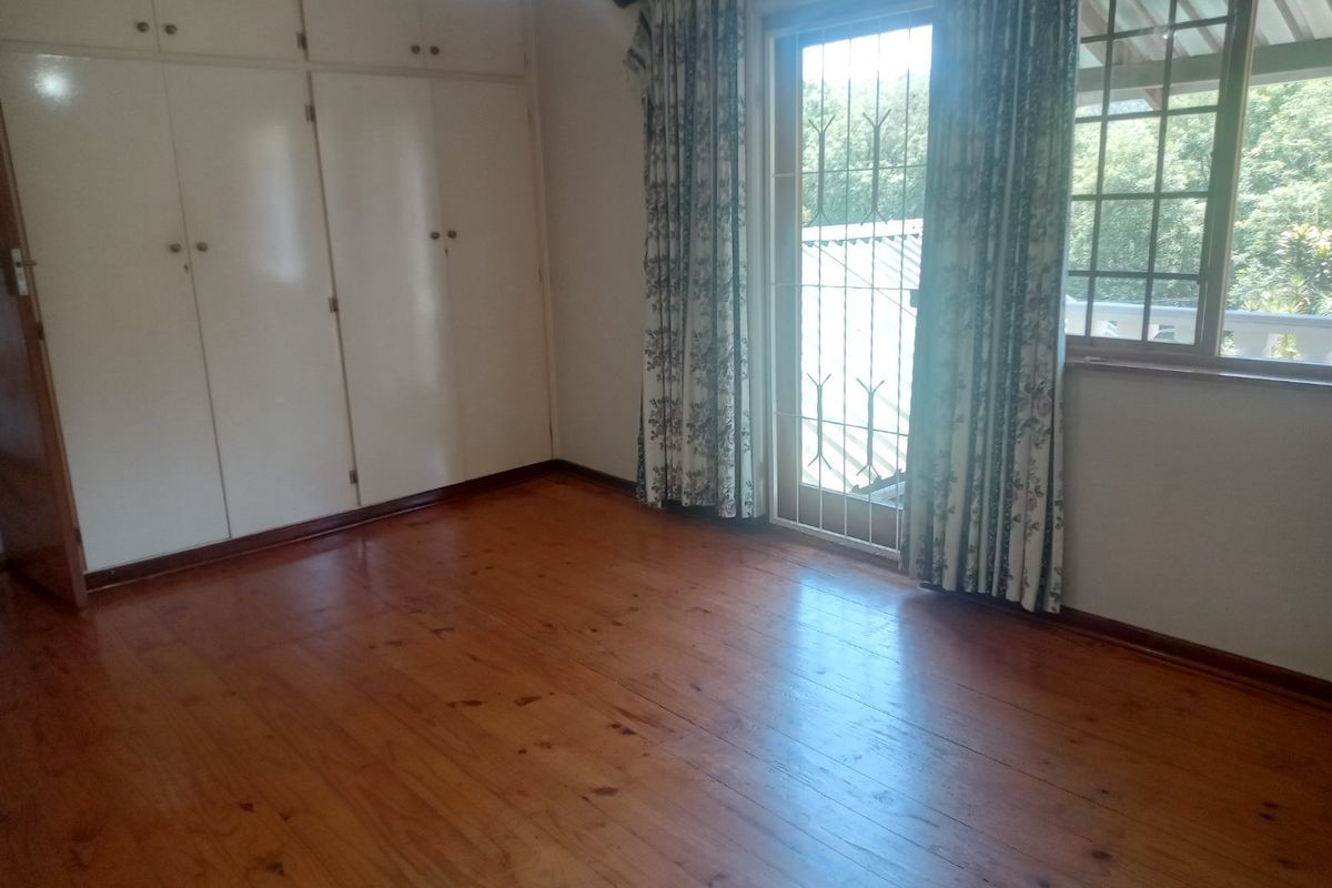 A bright, empty bedroom featuring polished timber flooring, extensive built-in cupboard storage, and direct access to an outdoor area via a security-gated door.