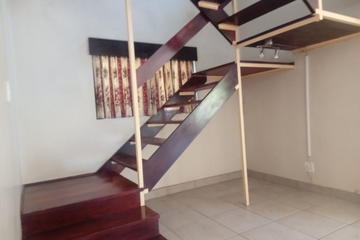 An open-plan living area featuring a wooden staircase leading to a mezzanine level with tiled flooring throughout.
