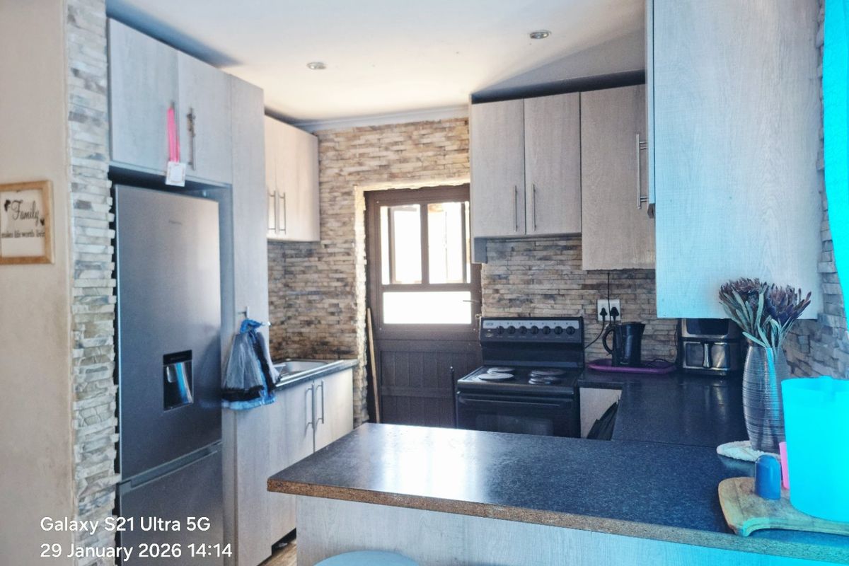 A functional kitchen featuring light wood-look cabinetry, stone veneer accent walls, dark laminate countertops, and a freestanding stove with direct access to the exterior.