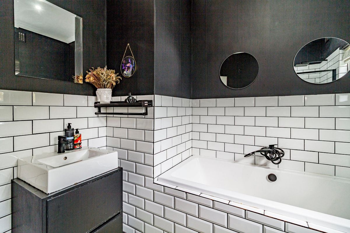 Modern bathroom featuring white subway tiles, black accent walls, a built-in bathtub, and a contemporary vanity with black tapware.