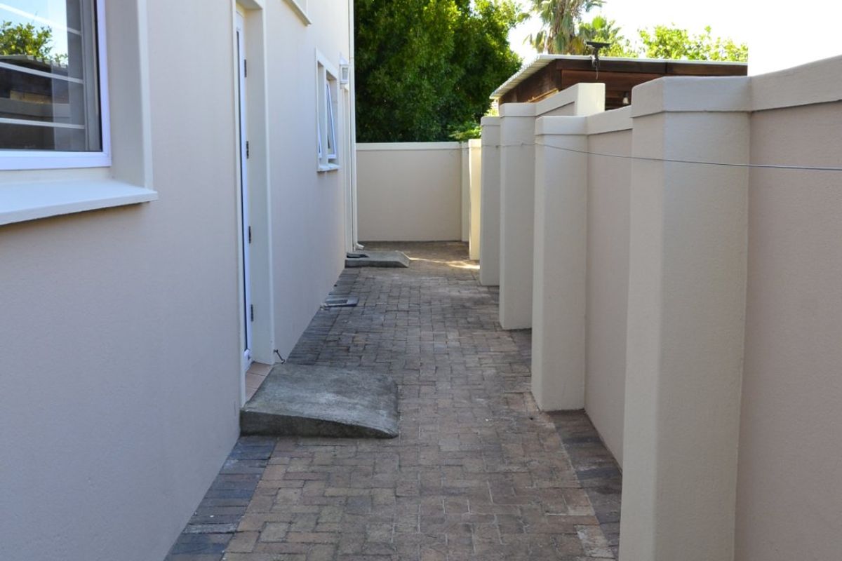 A side walkway featuring paved brick flooring, a boundary wall with pillars, and exterior wall-mounted lighting.