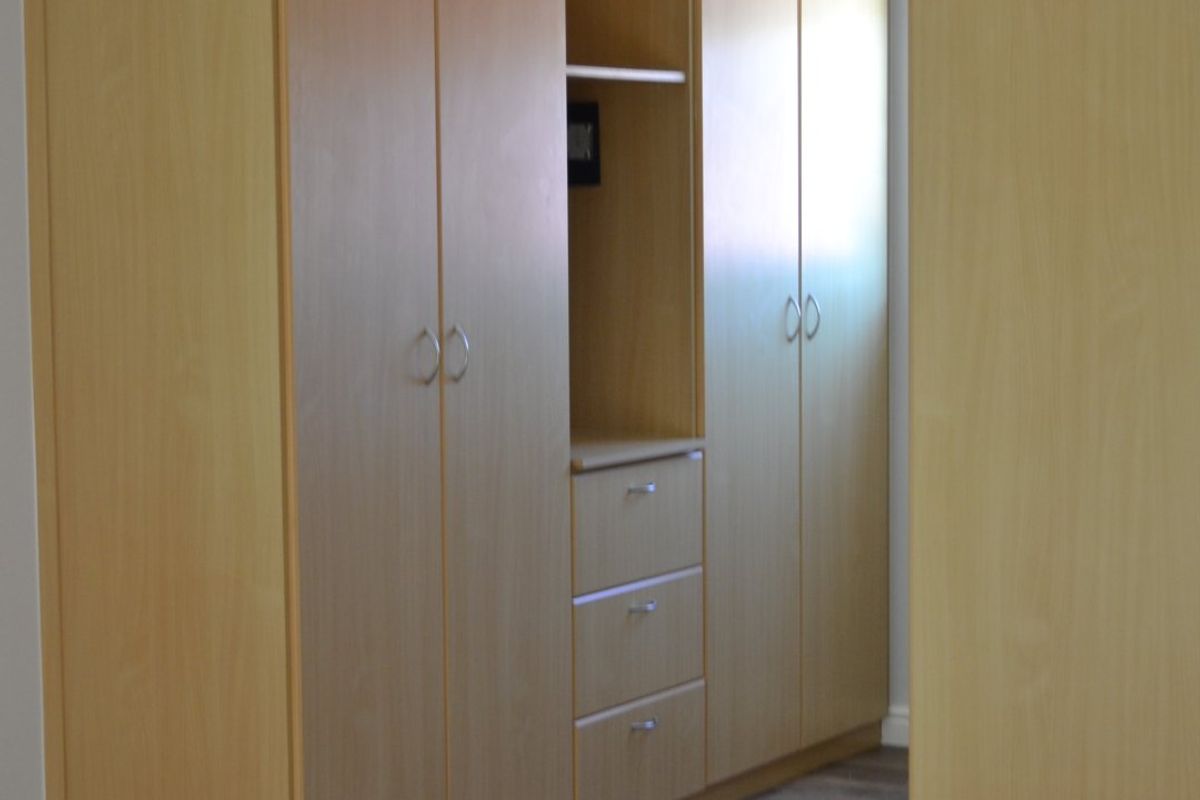 A bedroom featuring built-in light wood cabinetry with integrated shelving and drawers, complemented by wood-look laminate flooring.