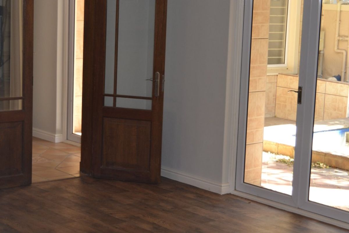 An empty living room featuring dark wood-look laminate flooring, classic timber-framed internal doors, and white uPVC sliding doors leading to an outdoor patio area.