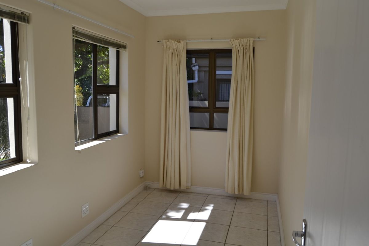 A bright, empty bedroom featuring neutral wall paint, tiled flooring, and multiple windows with aluminium frames.