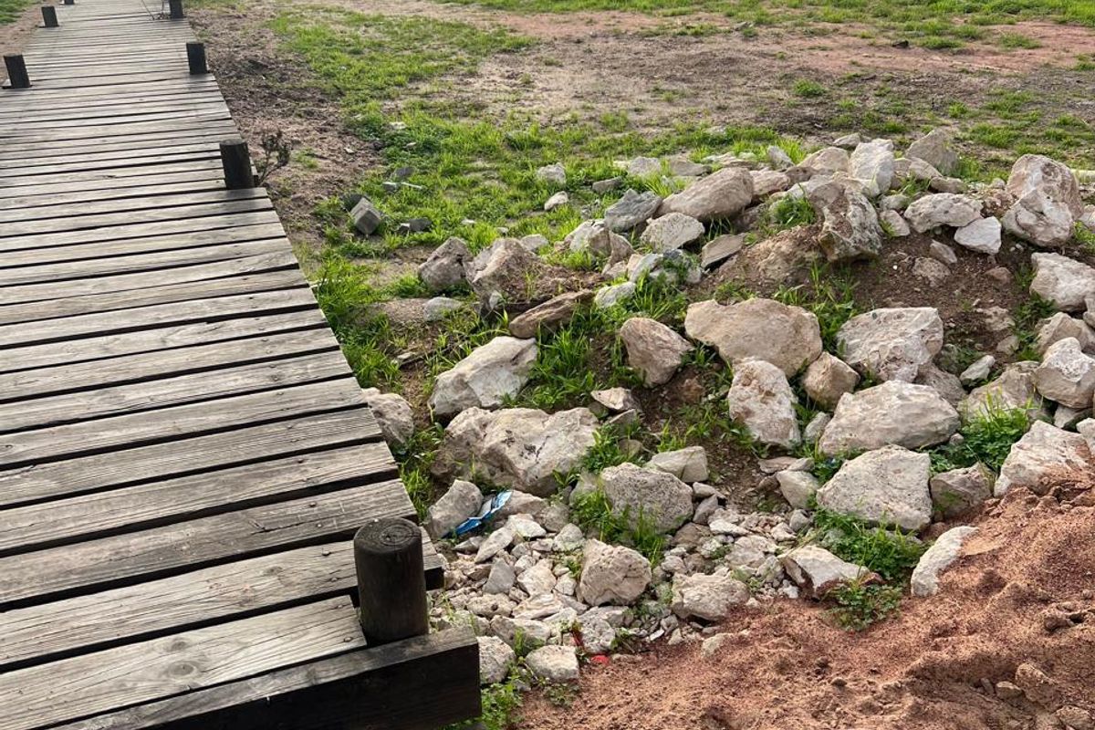 A coastal residential plot featuring a weathered timber boardwalk leading towards the ocean, with natural vegetation and rocky terrain.