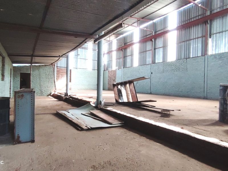 A large, open-plan utility or industrial space featuring exposed brick walls, concrete flooring, and a corrugated metal roof structure.
