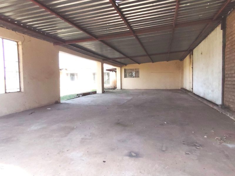 A large, covered outdoor patio area featuring a corrugated metal roof, concrete flooring, and exposed brickwork, offering a versatile space for renovation.