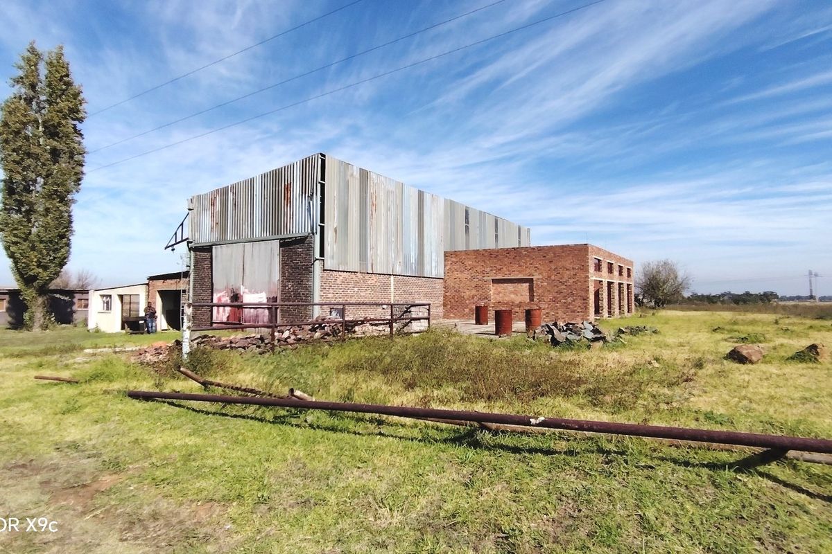 Exterior view of a large industrial-style structure featuring corrugated metal cladding and exposed brickwork, situated on a large open plot.