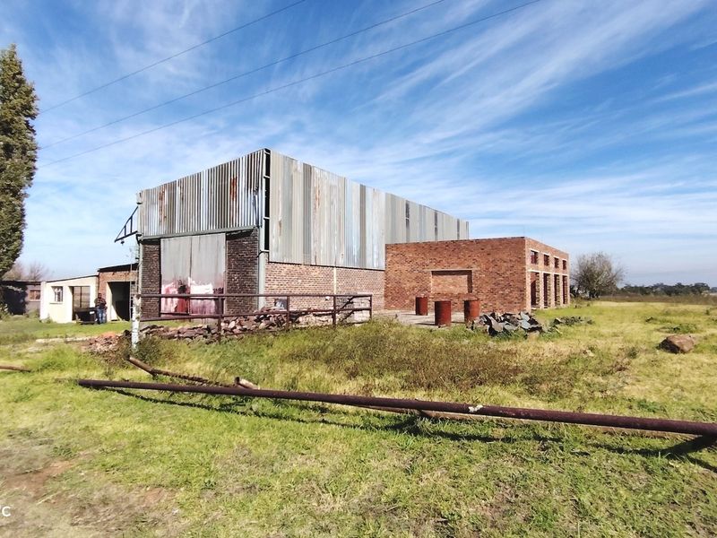 Exterior view of a large industrial-style structure featuring corrugated metal cladding and exposed brickwork, situated on a large open plot.