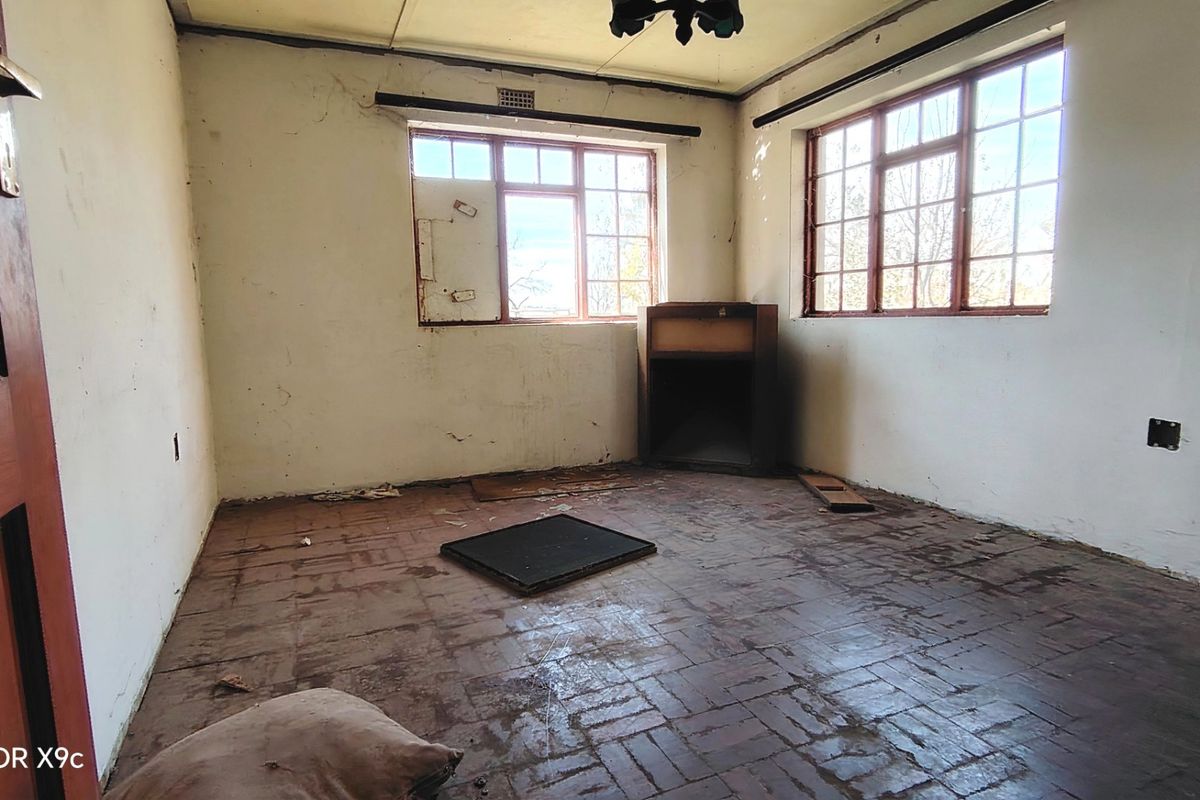 An empty bedroom featuring brick flooring, steel-framed windows, and a built-in fireplace, requiring significant renovation and cosmetic updates.