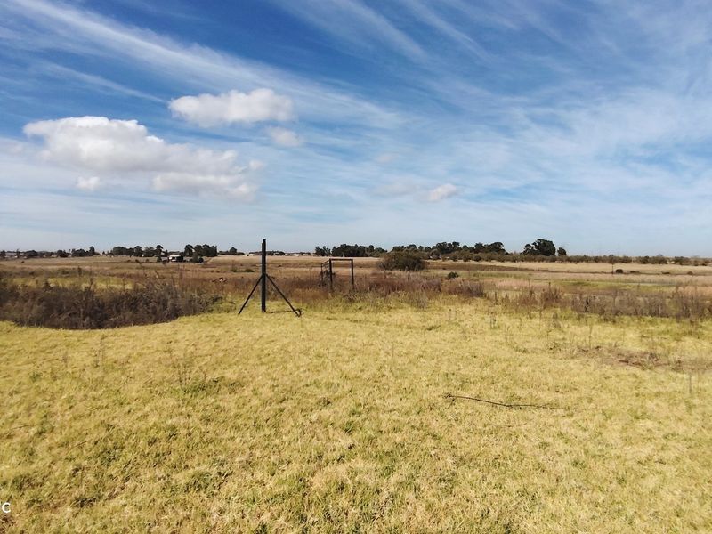 An expansive view of open, undeveloped land with natural grass and minimal fencing infrastructure.
