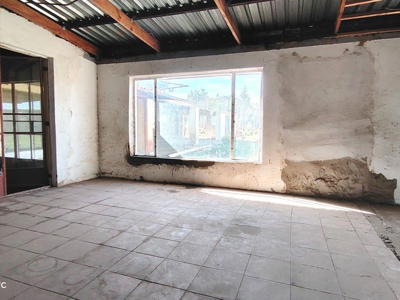 An empty, unfinished living area featuring exposed timber rafters, corrugated metal ceiling, tiled flooring, and large windows with views of the exterior.