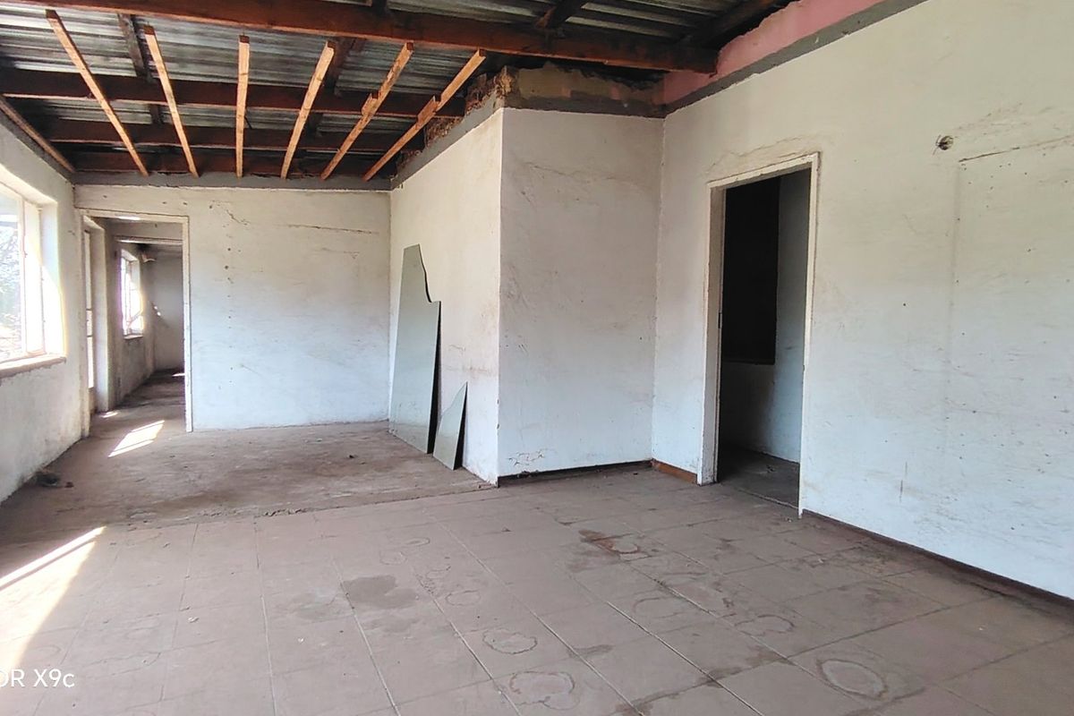 An empty, unfinished living area featuring exposed timber ceiling beams, tiled flooring, and basic wall finishes, requiring significant renovation and completion.