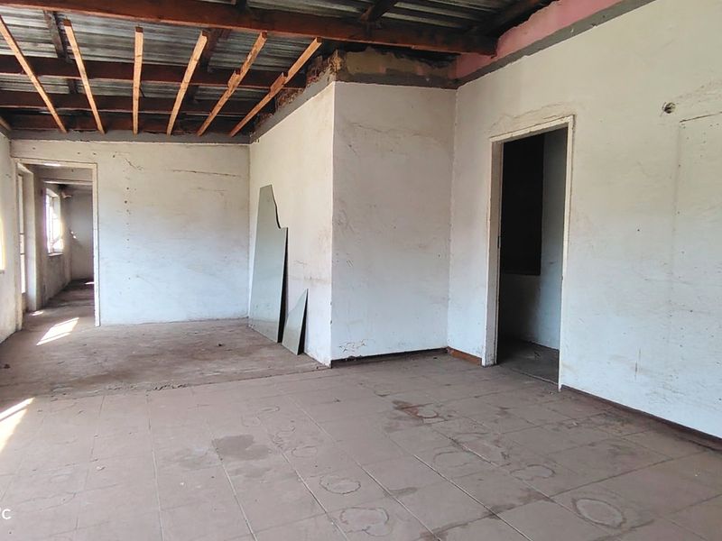 An empty, unfinished living area featuring exposed timber ceiling beams, tiled flooring, and basic wall finishes, requiring significant renovation and completion.