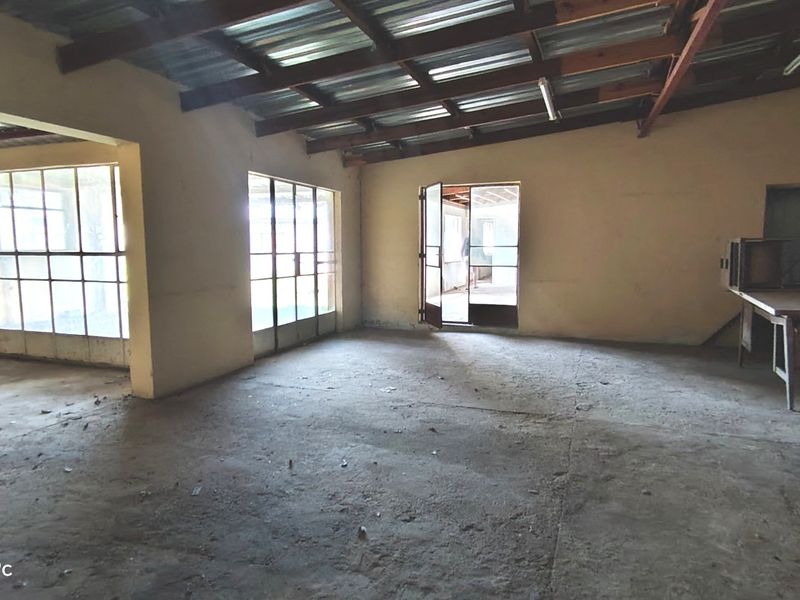 An expansive, unfinished utility space featuring exposed timber roof trusses, concrete flooring, and large steel-framed windows providing ample natural light.