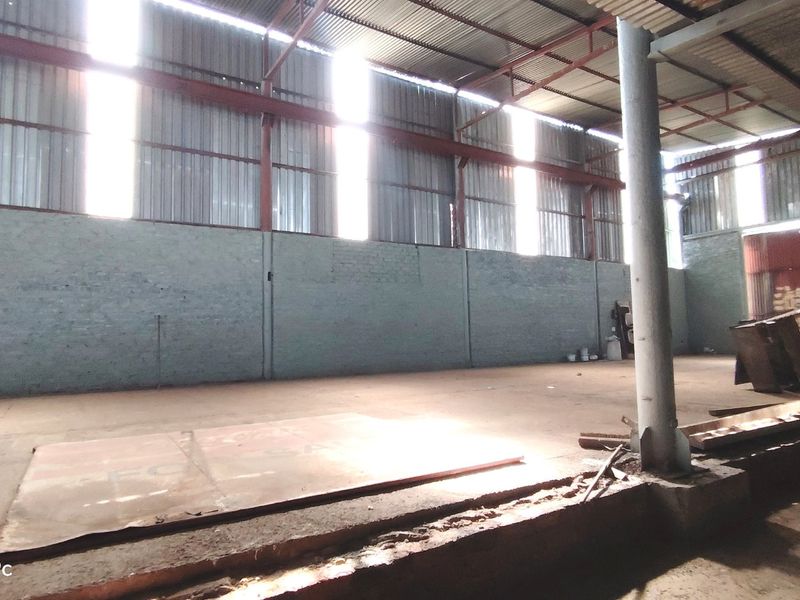 A large, open-plan utility or industrial space featuring exposed steel roof trusses, corrugated metal cladding, and painted brick walls with concrete flooring.