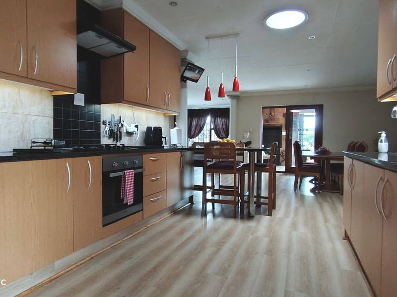 Open-plan kitchen and dining area featuring wood-finish cabinetry, stone countertops, built-in appliances, and modern laminate flooring.