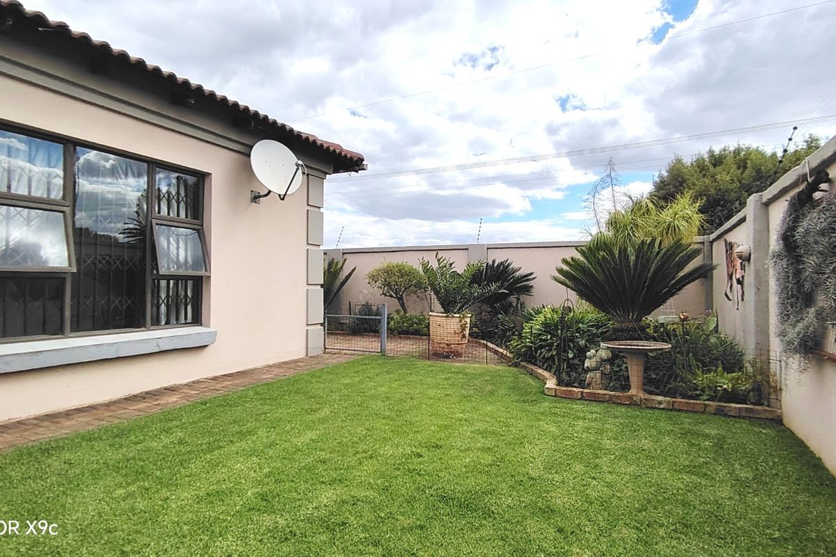 A well-maintained rear garden area featuring a manicured lawn, perimeter boundary walls with security fencing, and a tiled roof townhouse exterior.