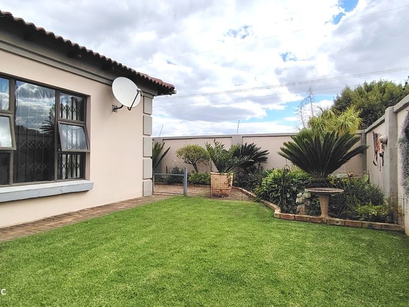 A well-maintained rear garden area featuring a manicured lawn, perimeter boundary walls with security fencing, and a tiled roof townhouse exterior.